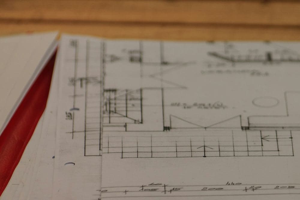Planos de arquitectura de una vivienda apilados sobre una mesa de madera