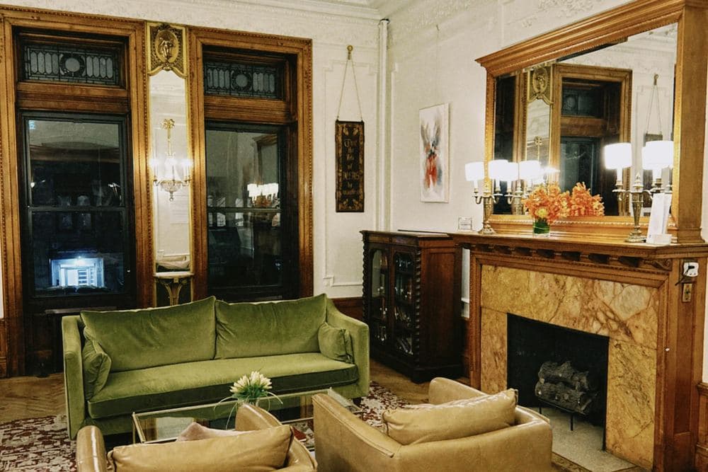 Salón señorial con chimenea de mármol, espejo dorado y sofá de terciopelo verde