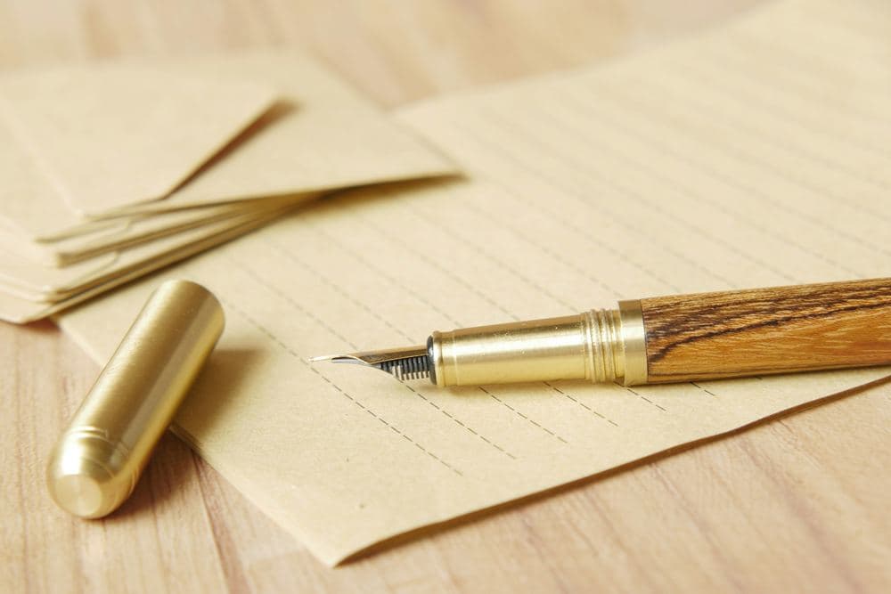 Pluma estilográfica de latón y madera apoyada sobre unos sobres de papel crema